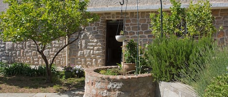 A stone building with a balcony, a hanging light fixture, and a variety of plants.