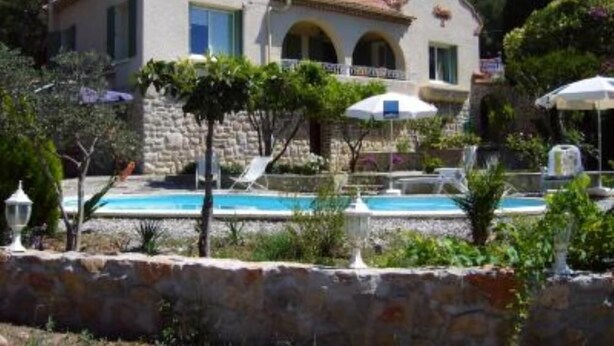 En villa i middelhavsstil med swimmingpool, stenvægge og et bjerg i baggrunden.