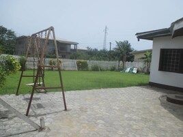 Un patio trasero con un parque infantil, un patio empedrado, una valla blanca y un césped.