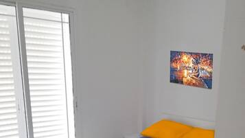 A bedroom with a bed, a window with blinds, and a painting on the wall.