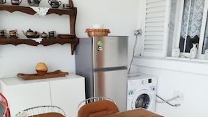 A kitchen with a wooden table, metal chairs, a refrigerator, a washing machine, and shelves with kitchenware. - Hanioti Apartment (Kassandra)