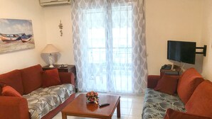 A living room with two red sofas, a wooden coffee table, a TV on a stand, and a window with patterned curtains. - Hanioti Apartment (Kassandra)