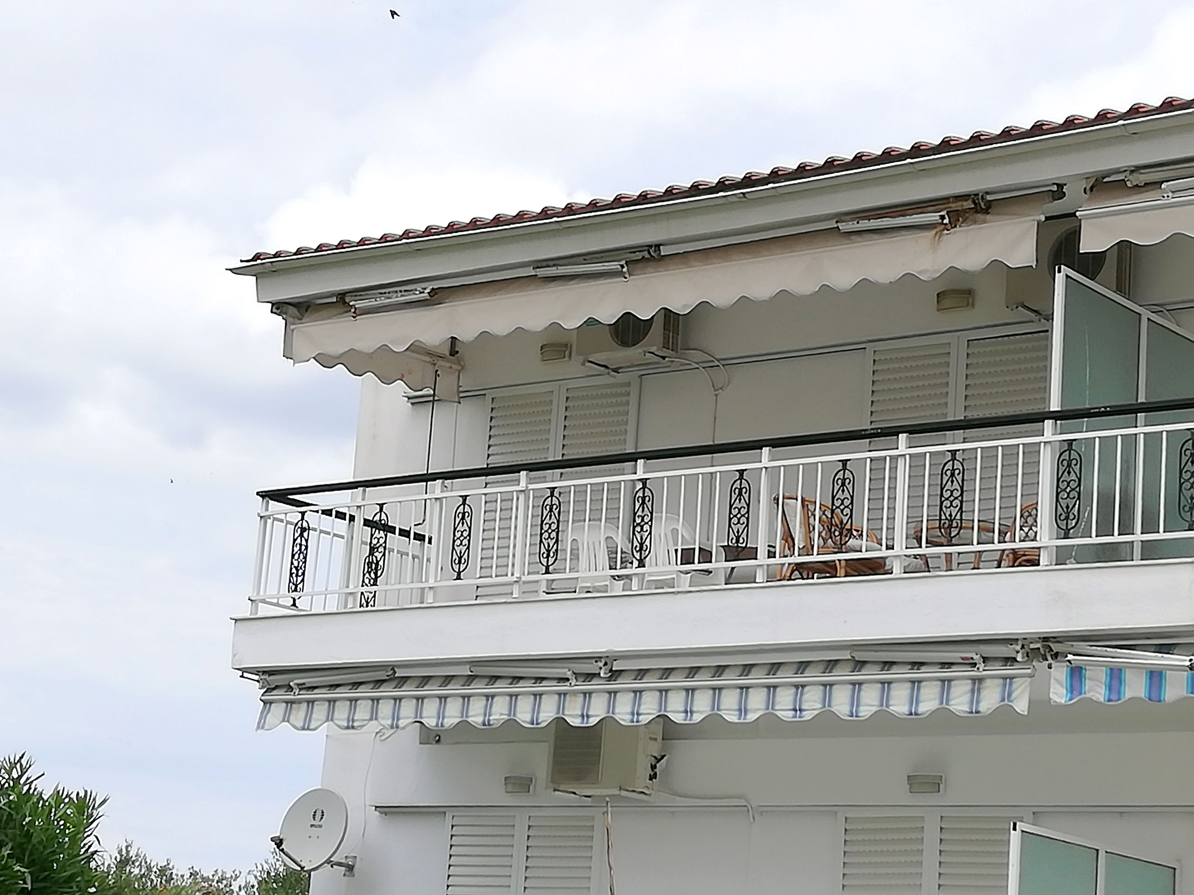 A two-story building with a balcony featuring white railings and a satellite dish.