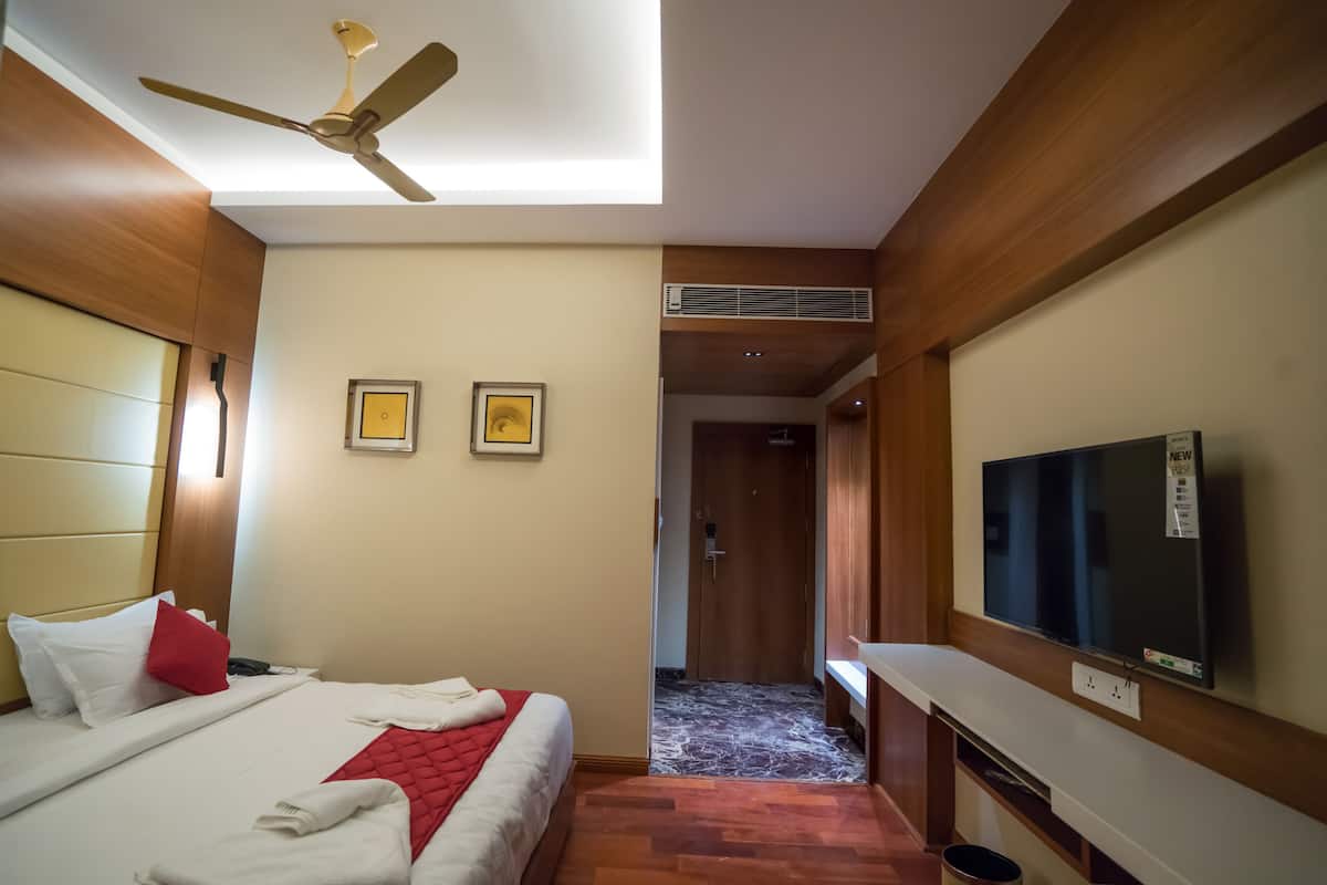 Ein Hotelzimmer mit Bett, Deckenventilator, Fernseher und einem zur anderen Zimmer führenden Gang.