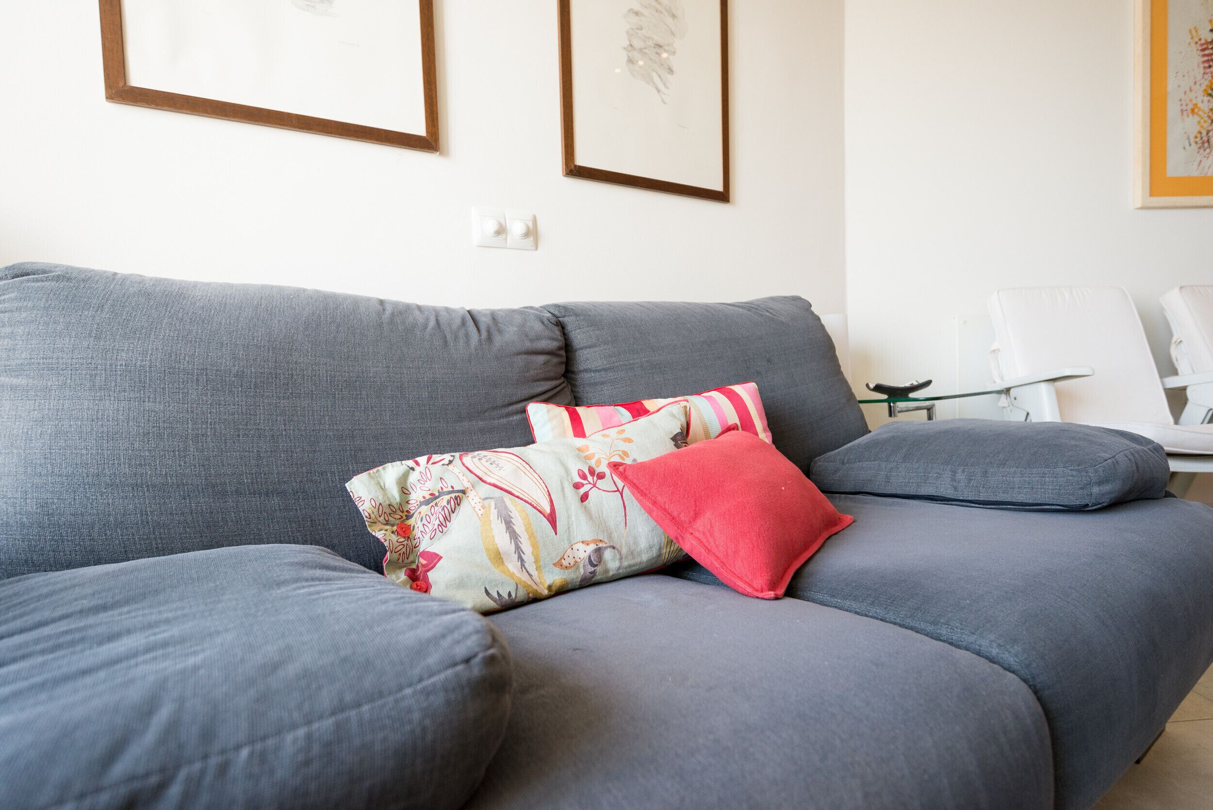 Un sofá gris con cojines estampados y una almohada roja.