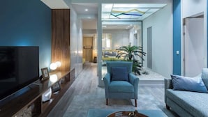 A modern living room with a TV, seating, and a glass partition leading to a bedroom.