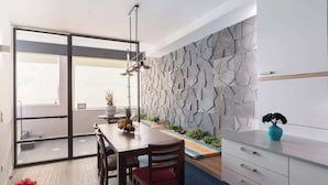 A modern kitchen with a geometric backsplash, a dining area with a wooden table and chairs, and a view through a glass door to an outdoor space.
