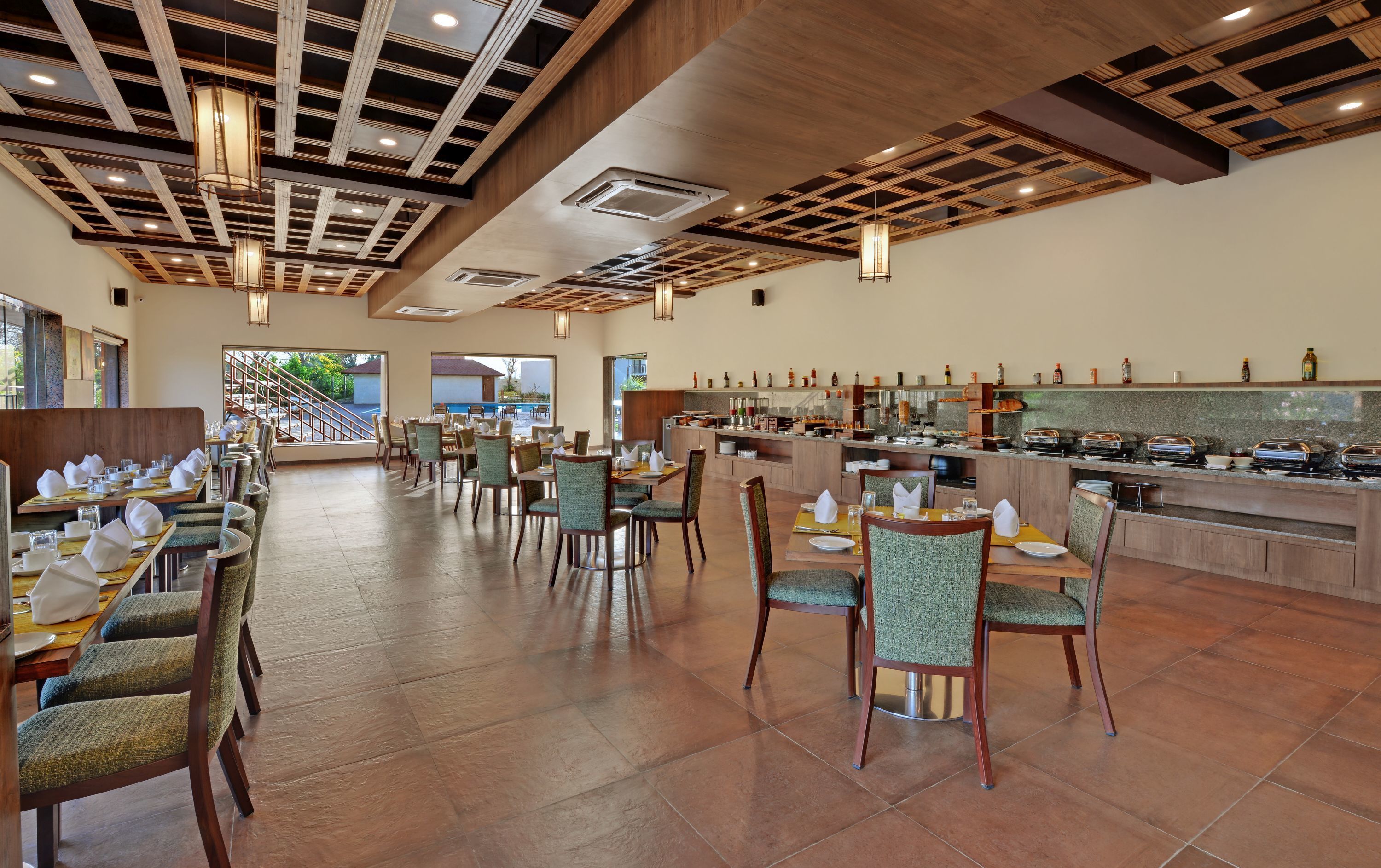 Un comedor amplio con mesas y sillas largas, un mostrador de buffet con diversas opciones de comida, y vistas al exterior a través de grandes ventanales.