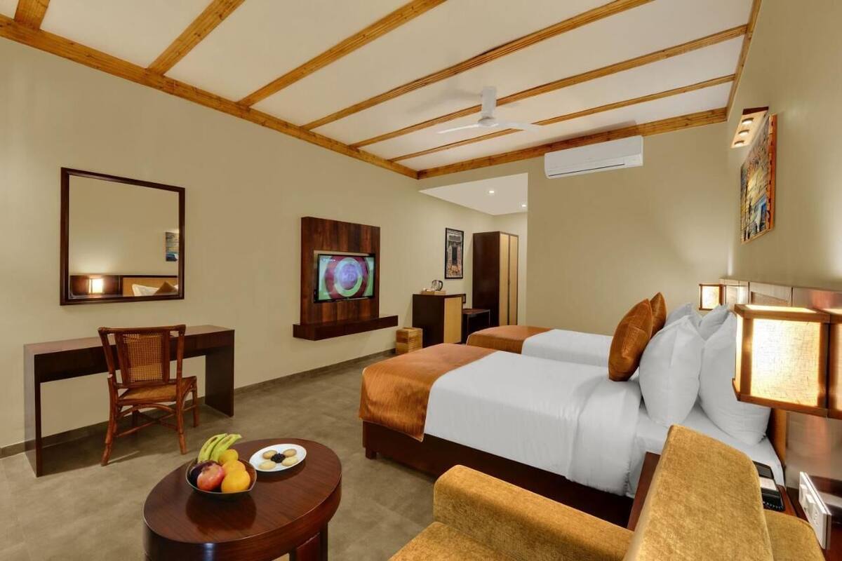 A hotel room with two beds, a desk, a chair, a TV, and a fruit bowl.