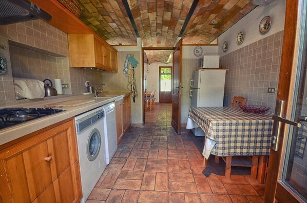 A compact kitchen with a washing machine, a stove, and a dining area with a checkered tablecloth. - Panoramic villa with pool, internet wifi, large garden, 60 km from Rome (Casperia)