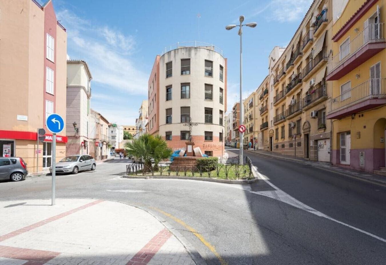 A street view with a roundabout, buildings, and a clear sky.