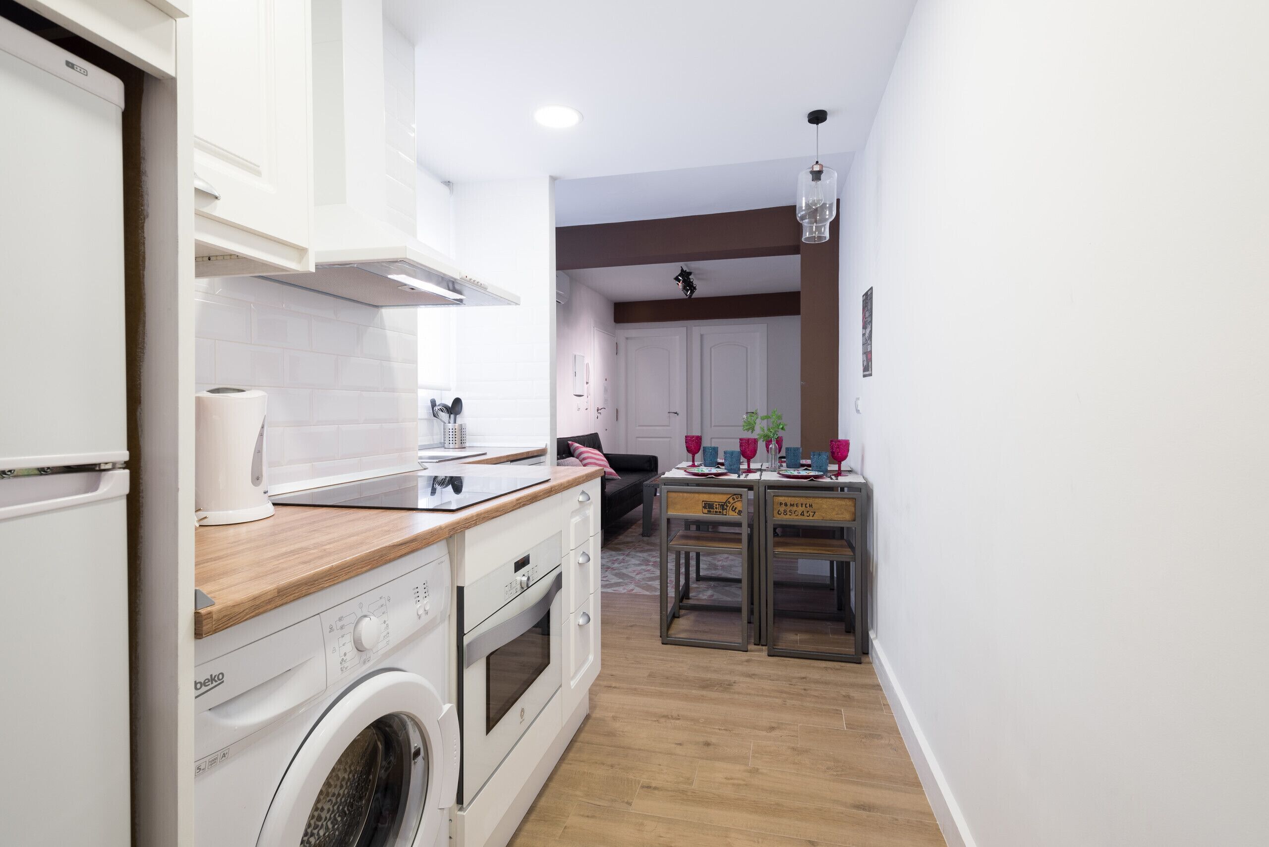 A compact kitchen with a washing machine, oven, and wooden countertop.