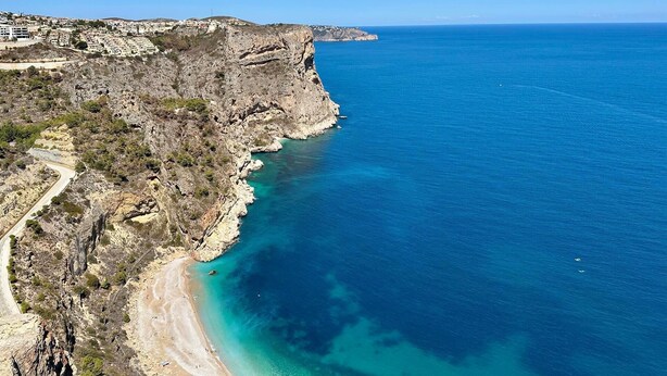 Paisagem costeira com um litoral rochoso, mar azul cristalino e uma estrada serpenteando pela costa.