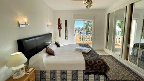 Quarto com cama, mesa de cabeceira, luminária, ventilador de teto e vista para o exterior.
