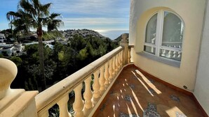 Uma varanda com vista para uma cidade costeira, uma palmeira e um chão de azulejos.