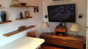 A modern living room with a flat-screen TV, wooden shelves, a dining table, and a cabinet with drawers. - Stunning self contained 1 bedroom flat in the heart of Putney.  (London)