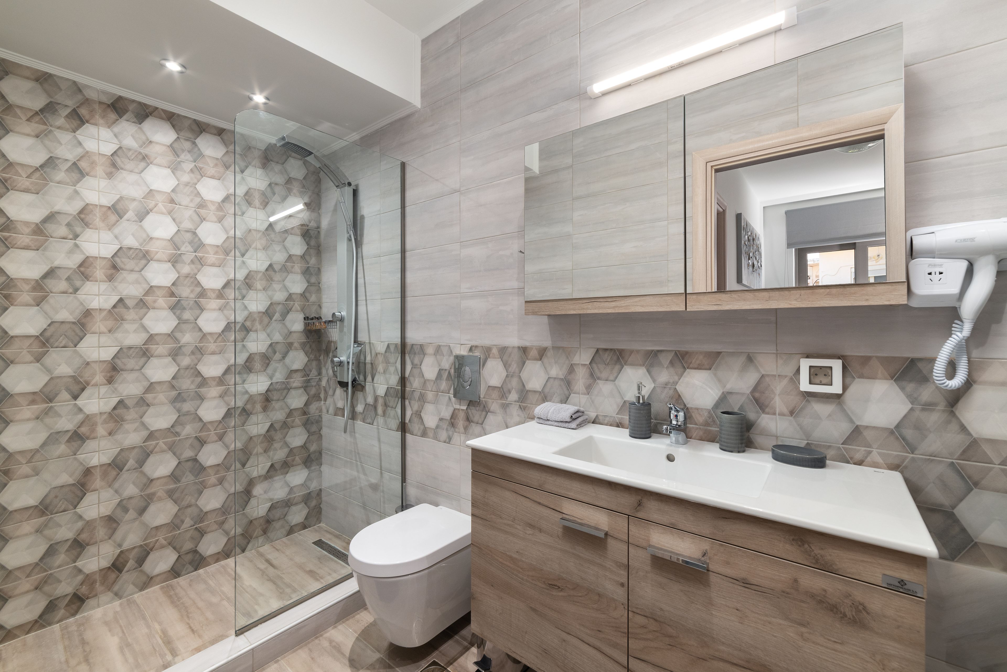 A modern bathroom with a glass shower enclosure, a white toilet, and a wooden vanity with a mirror above.
