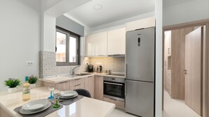 A modern kitchen with stainless steel appliances, a dining area with a table set for two, and light wood cabinetry. - Rhodes Luxury Apartments (Rhodes)