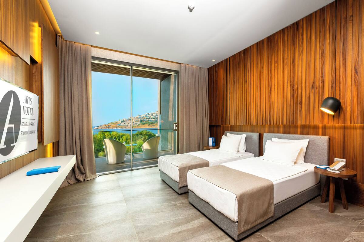 Habitació d'hotel amb dos llits, una taula, una cadira, un balcó amb vistes i una paret de fusta.