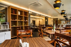 L’intérieur d’un restaurant est aménagé avec des meubles en bois, des luminaires suspendus et un mur décoratif agrémenté d’étagères.