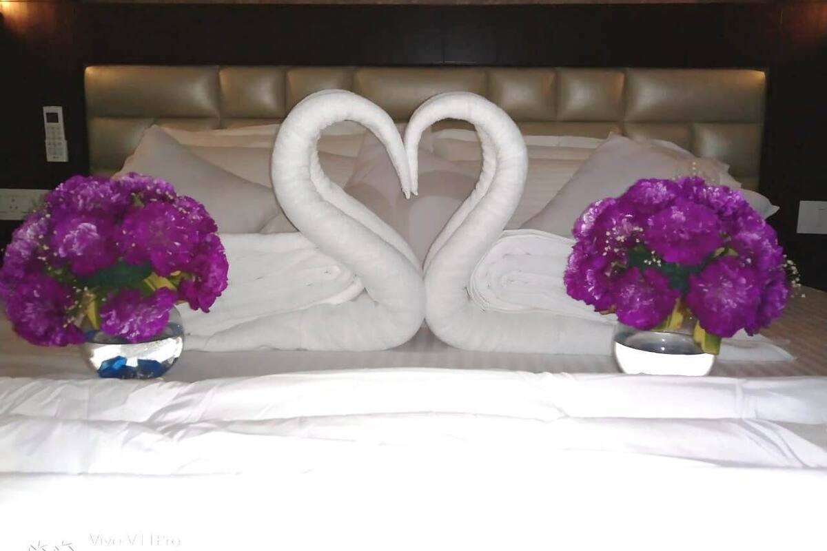 Un lit décoré de serviettes disposées en forme de cœur et agrémenté de deux vases remplis de fleurs violettes.