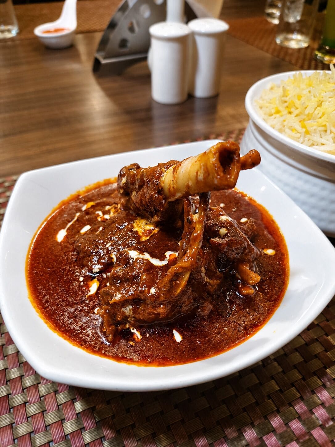 A plate of meat with sauce, a bowl of rice, and salt and pepper shakers on a table.