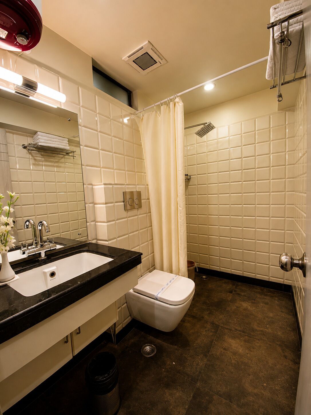 A bathroom with a white tiled wall, a black sink, a toilet, and a shower area.