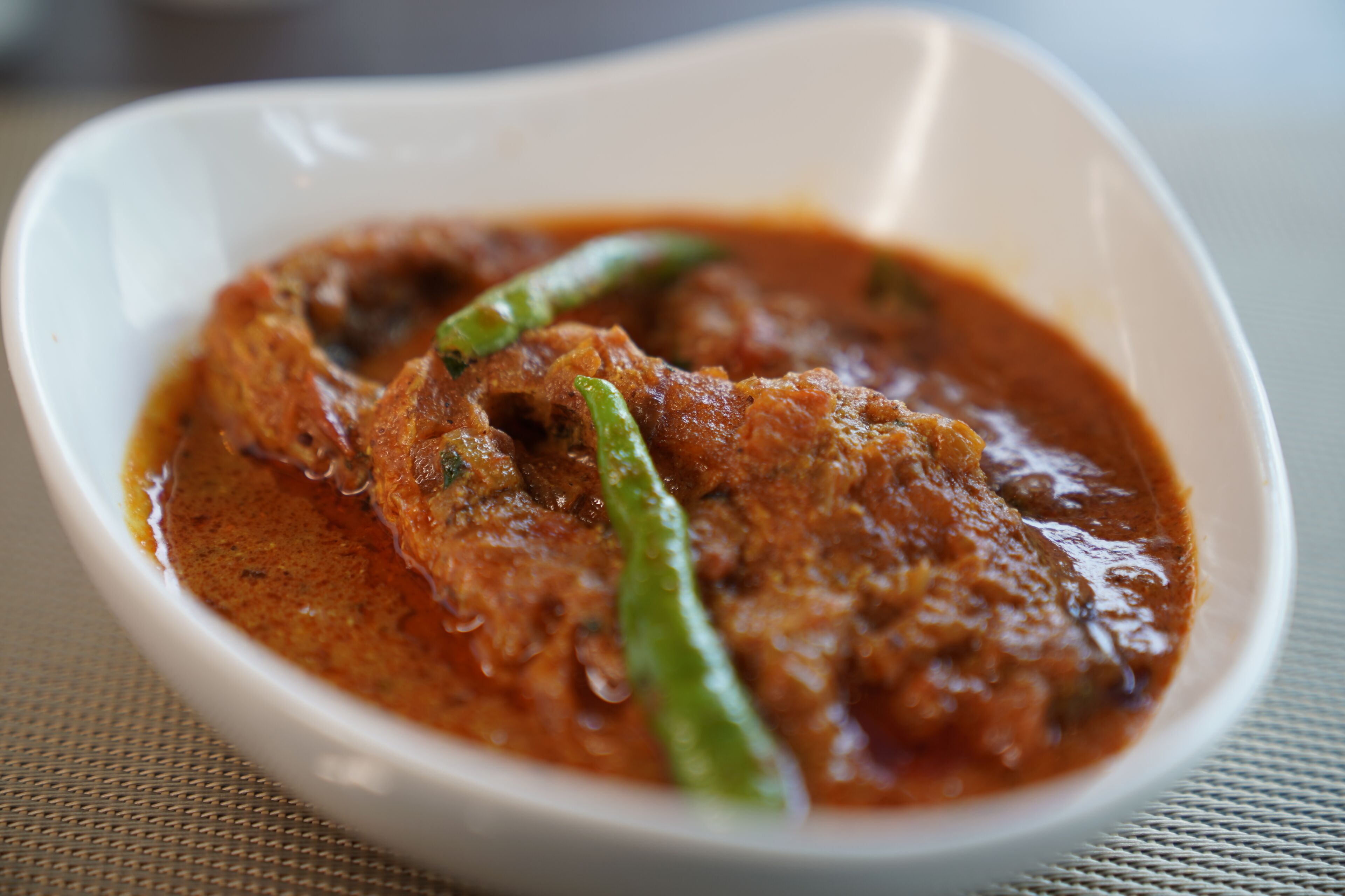 Un tazón blanco con curry, carne y chiles verdes.