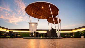 A spacious outdoor area with a modern architectural design, featuring a central wooden structure with multiple circular platforms and seating arrangements.