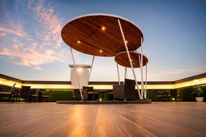 Un amplio espacio al aire libre con diseño arquitectónico moderno, que presenta una estructura de madera central con múltiples plataformas circulares y zonas de estar.