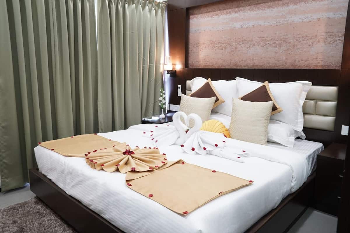 Un lit bien fait, avec une couette blanche, des oreillers beige et blancs, et des objets décoratifs, notamment une serviette en forme de cygne et un arrangement floral.