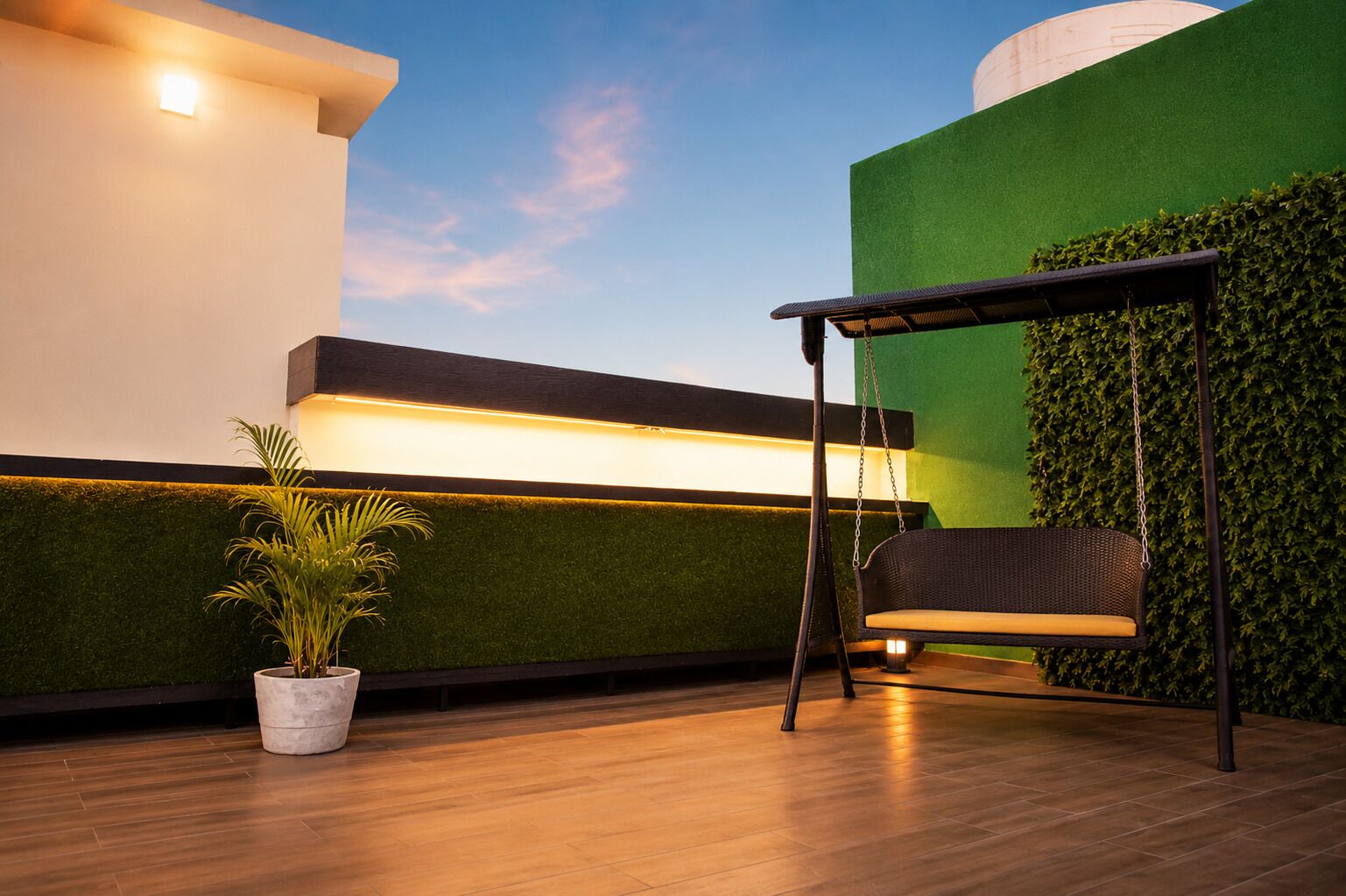 A modern outdoor seating area with a swing chair, a potted plant, and a wall with a green hedge.