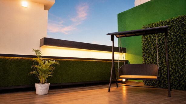 A modern outdoor seating area with a swing chair, a potted plant, and a wall with a green hedge.