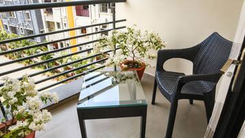 Een balkon met een glazen tafel, een rieten stoel en potplanten.