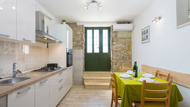 A compact kitchen with white cabinets, a wooden countertop, and a dining area with a green tablecloth. - Downtown Split City Apartment (Split)