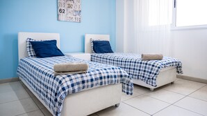 A room with two beds, each with a blue and white checkered bedspread and matching pillows, against a light blue wall. - Narcissos Nissi Beach Apartment D9 (Ayia Napa)