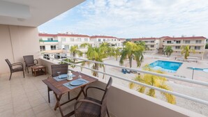 A balcony with a table and chairs, overlooking a swimming pool and buildings. - Narcissos Nissi Beach Apartment D9 (Ayia Napa)
