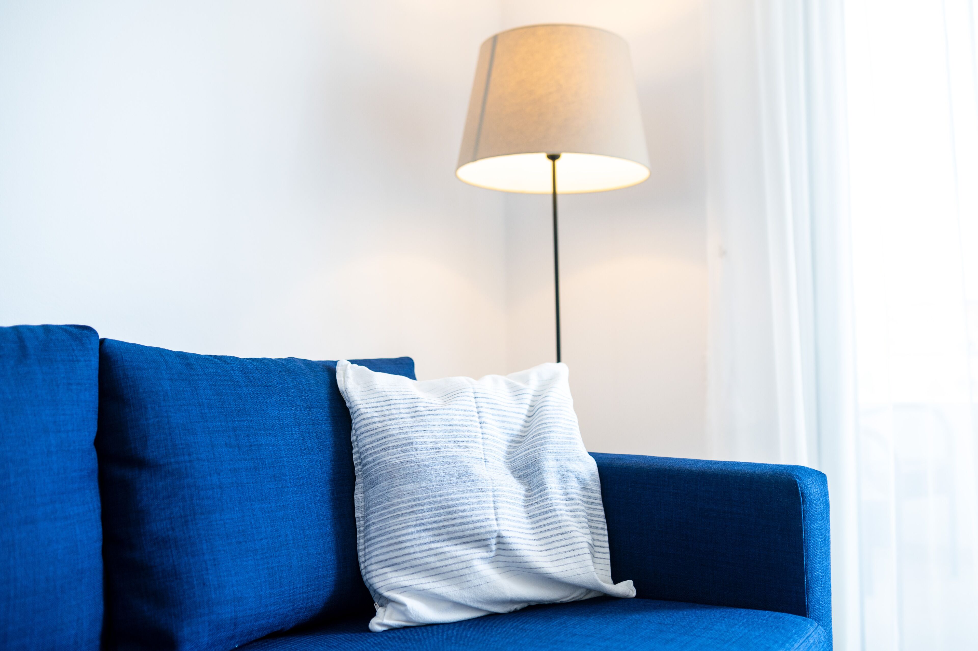 A blue sofa with a striped pillow and a floor lamp.