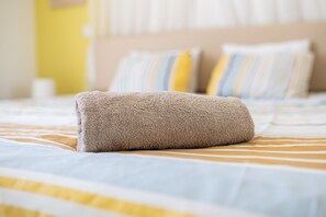 A neatly made bed with striped bedding and a folded towel on top. - Narcissos Nissi Beach Apartment D9 (Ayia Napa)