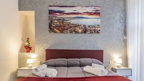 Une chambre d’hôtel avec un grand lit, deux tables de chevet avec des lampes, un plaid rouge et un tableau représentant un paysage urbain accroché au mur.