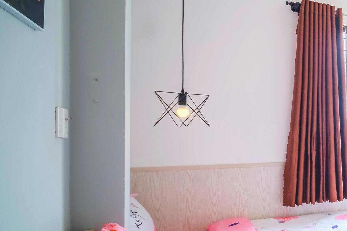 Une chambre à coucher avec une tête de lit en bois, un luminaire suspendu et une fenêtre ornée de rideaux bruns.