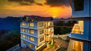 Un edificio de varios pisos con balcones y un atardecer al fondo.
