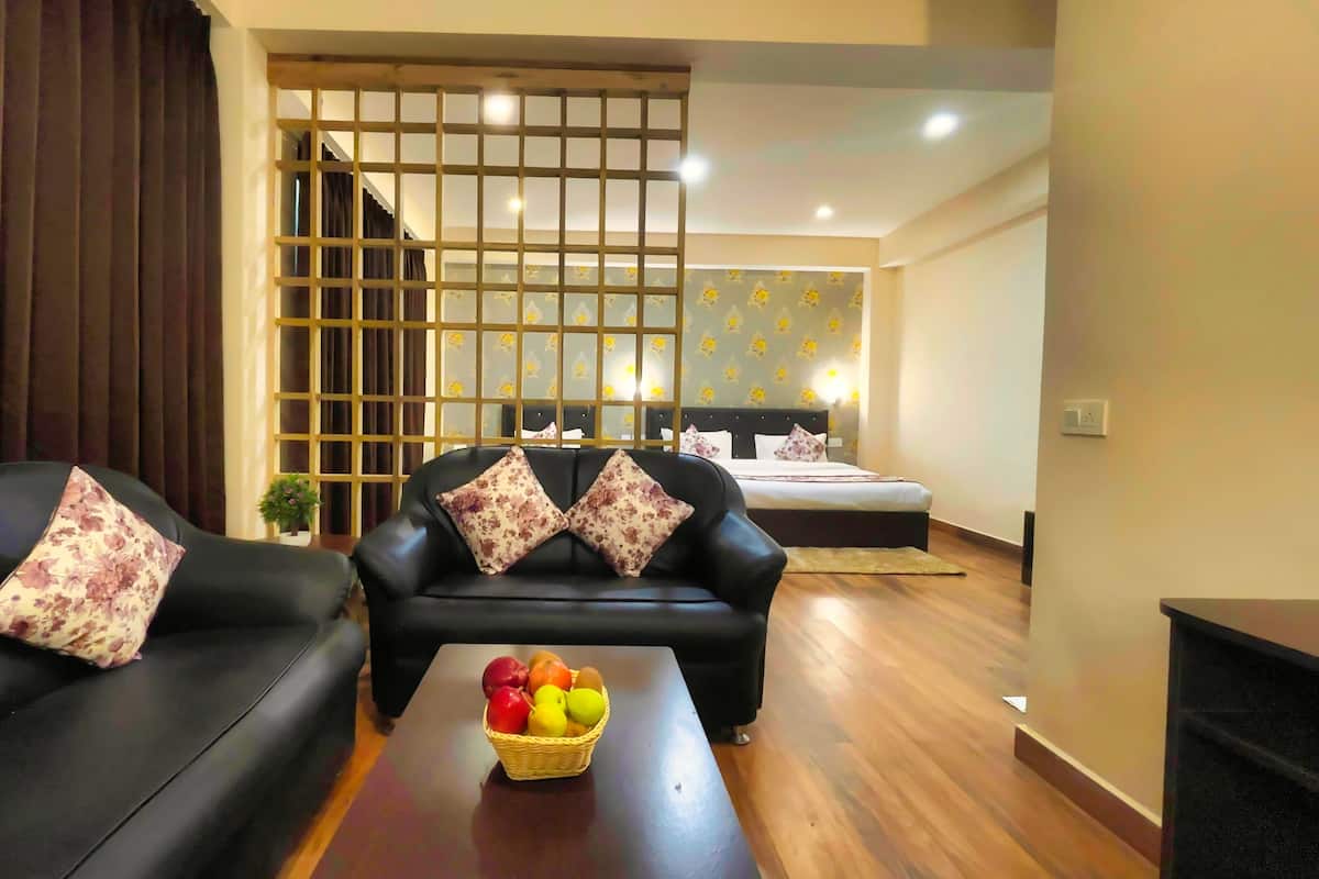 A hotel room with a sofa, a coffee table with fruit, a bed, and a decorative partition.