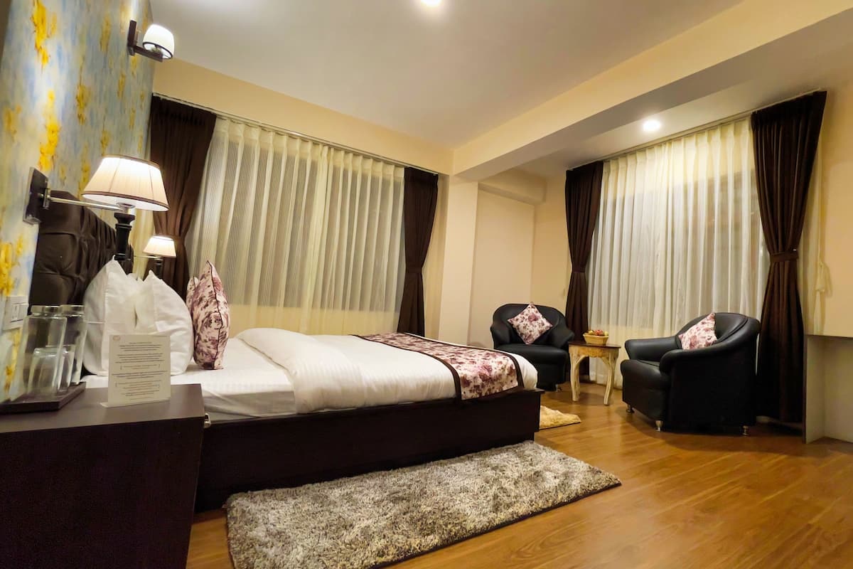 A hotel room with a bed, two armchairs, a desk, a TV, and a small table with a fruit bowl.