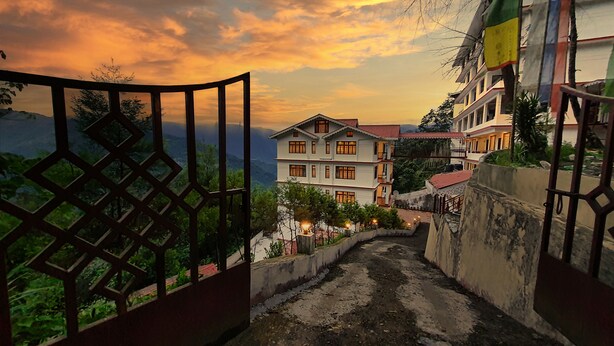 Un edificio tradicional de varios pisos con techo rojo, rodeado de vegetación y un paisaje montañoso.
