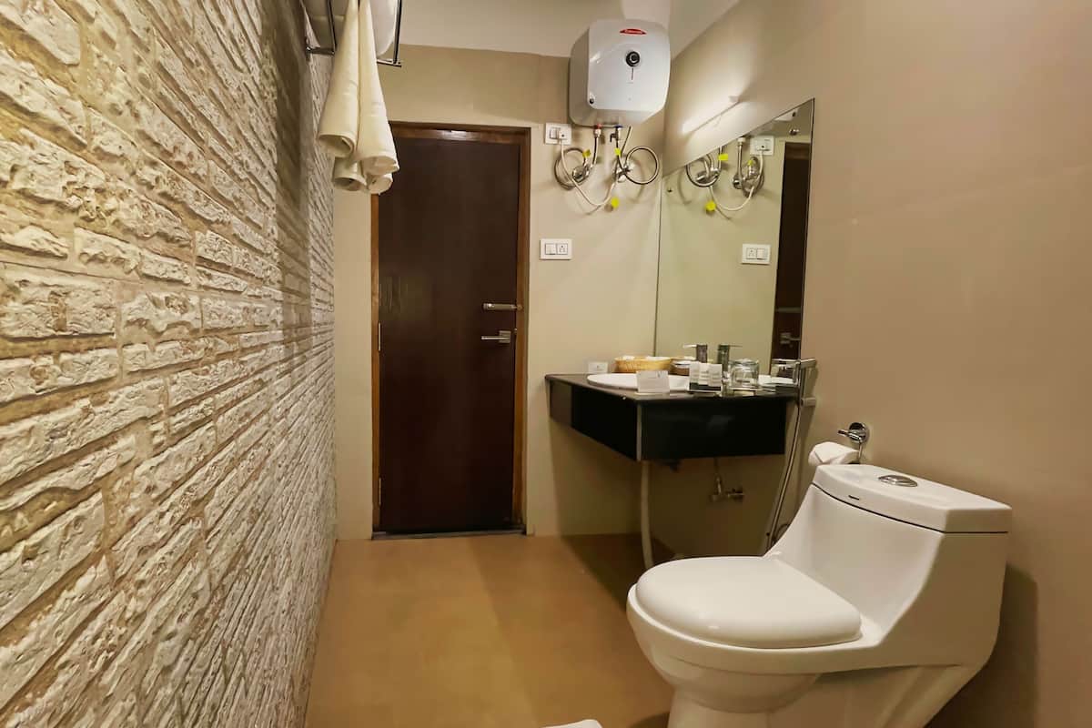A bathroom with a stone wall, a wooden door, a white toilet, a sink with a mirror, and a towel rack.