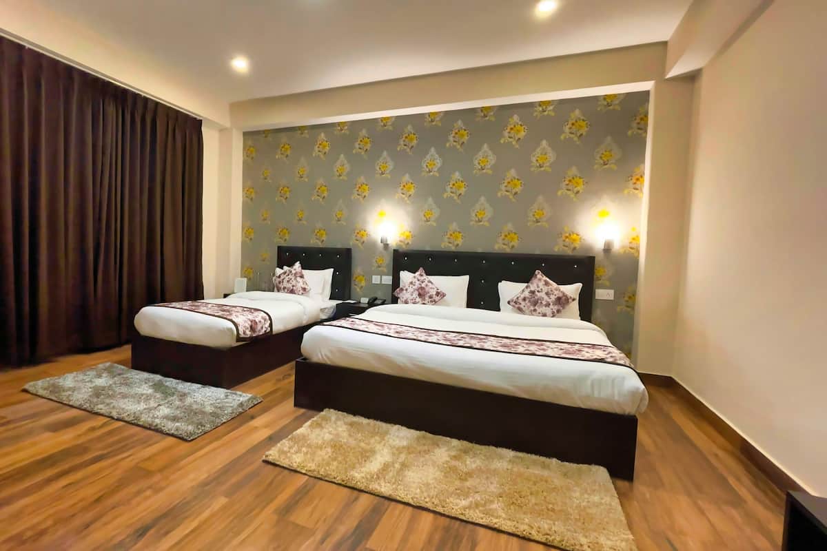 A hotel room with two beds, wooden flooring, a large window with curtains, and a floral wallpaper.