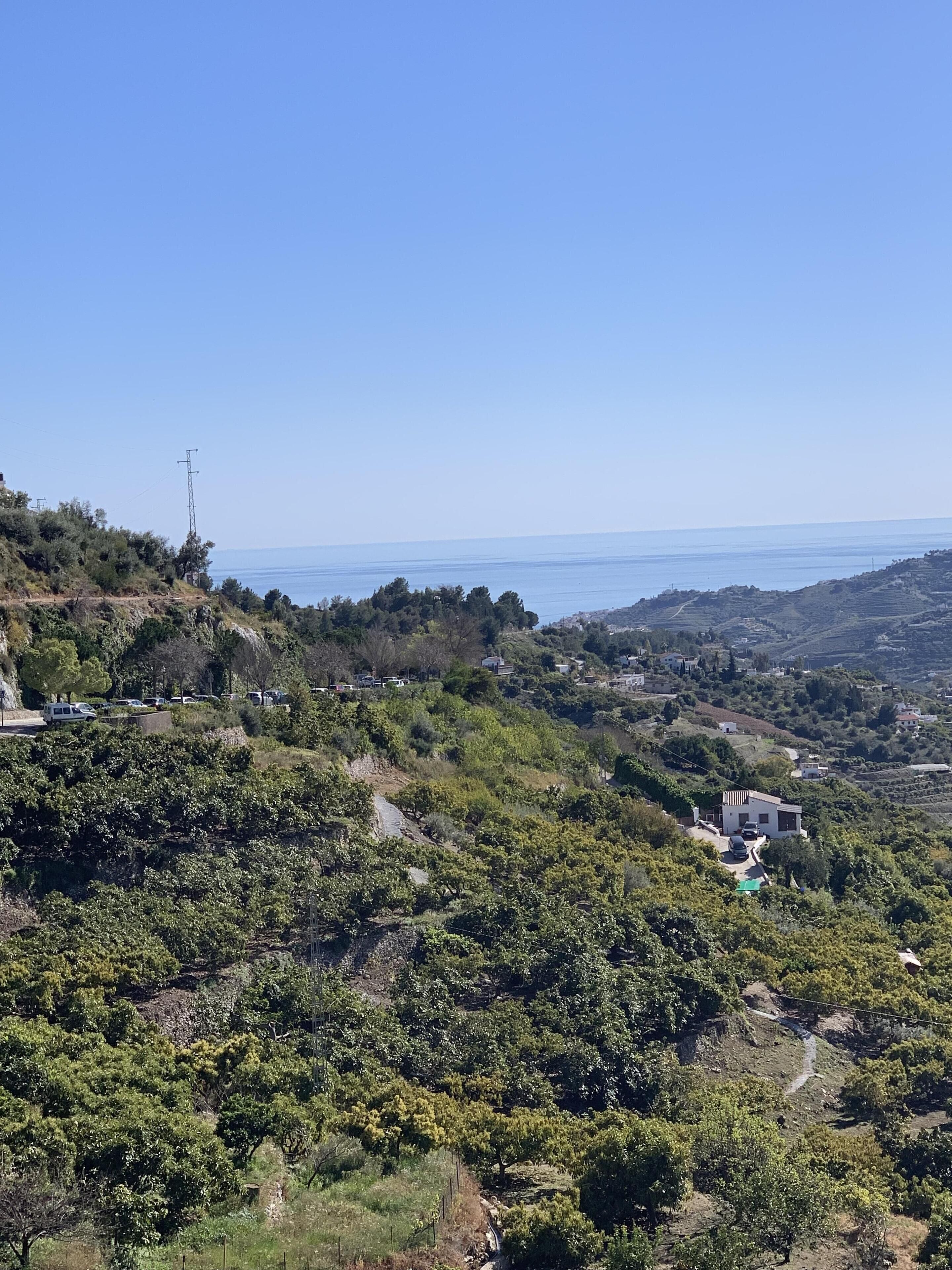 A hilly landscape with a clear view of the sea, a few buildings, and a power line.