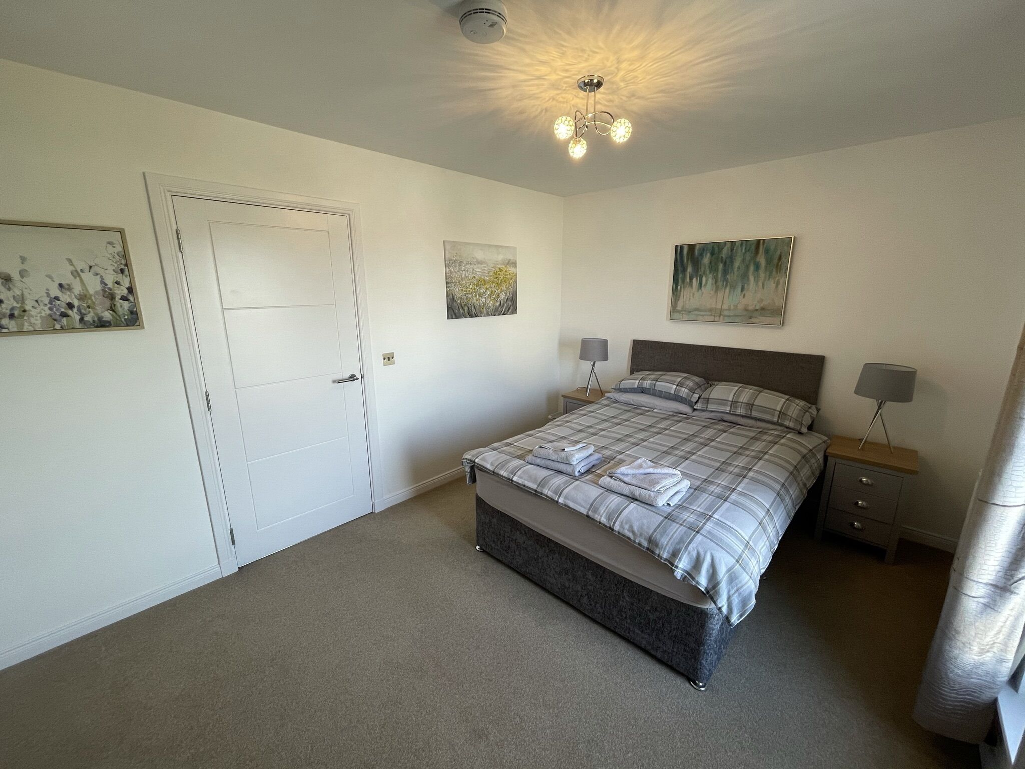 Un dormitorio con una cama, dos mesitas de noche, una puerta y una lámpara en el techo.