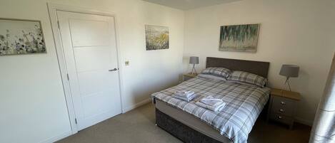 Un dormitorio con una cama, dos mesitas de noche, una puerta y una lámpara en el techo.